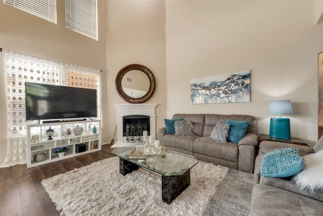 living area with a fireplace with raised hearth, a towering ceiling, and wood-type flooring