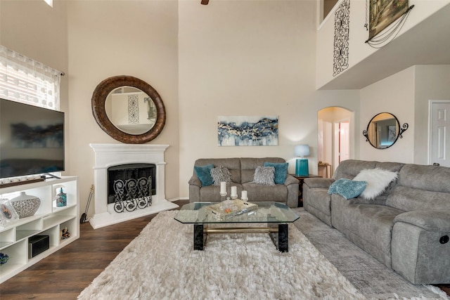 living room featuring a high ceiling, arched walkways, a fireplace with raised hearth, and dark wood finished floors