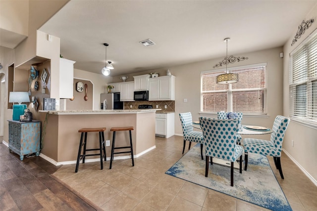 kitchen with backsplash, black microwave, white cabinetry, stainless steel fridge, and visible vents