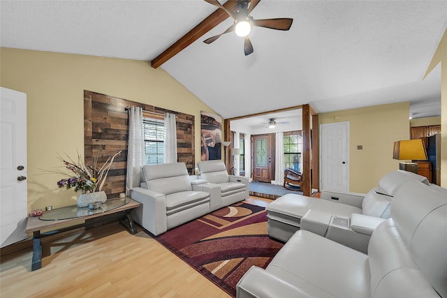 living area featuring a wealth of natural light, wood finished floors, vaulted ceiling with beams, and a ceiling fan
