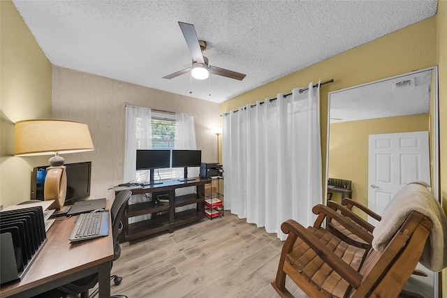 office area with a textured ceiling, visible vents, light wood-style floors, and a ceiling fan