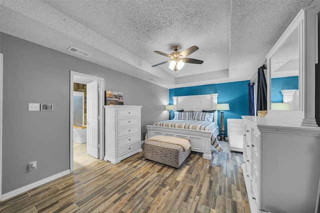 bedroom featuring a tray ceiling, wood finished floors, a textured ceiling, baseboards, and visible vents