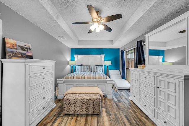 bedroom with dark wood-style flooring, a textured ceiling, visible vents, ceiling fan, and a tray ceiling