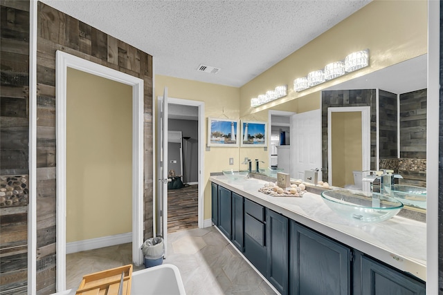full bath featuring double vanity, visible vents, a sink, and a textured ceiling