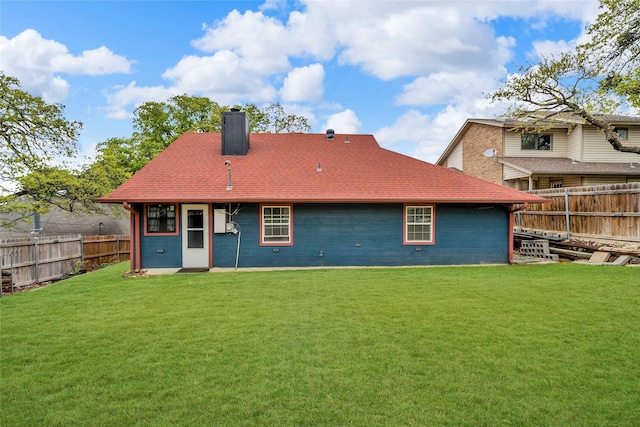 back of property with roof with shingles, fence private yard, a yard, and a chimney