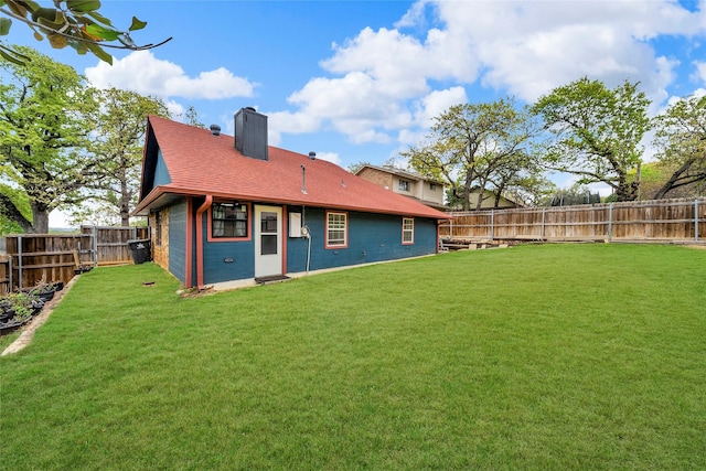 rear view of property with a fenced backyard, a chimney, roof with shingles, and a yard