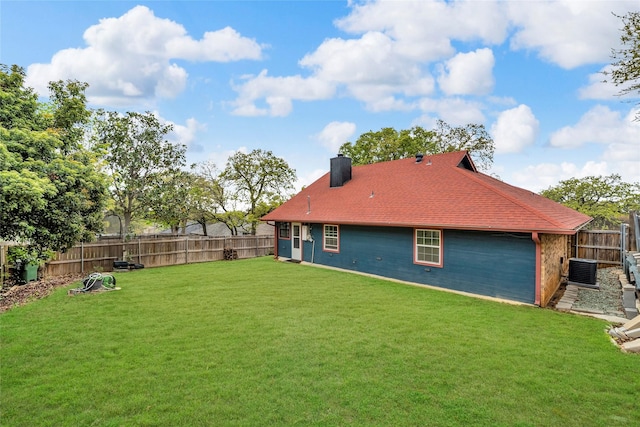 back of property with a fenced backyard, a lawn, a chimney, and central AC