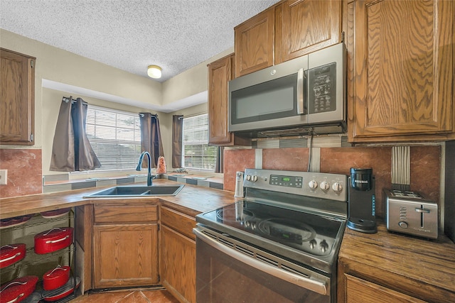 kitchen with a textured ceiling, wood counters, stainless steel appliances, tasteful backsplash, and a sink