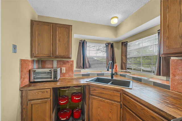 kitchen featuring a sink, brown cabinets, a toaster, wood counters, and decorative backsplash