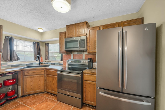 kitchen featuring light tile patterned flooring, a sink, appliances with stainless steel finishes, a textured ceiling, and brown cabinetry