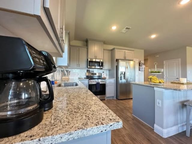 kitchen featuring light stone counters, backsplash, a sink, stainless steel appliances, and dark wood-type flooring