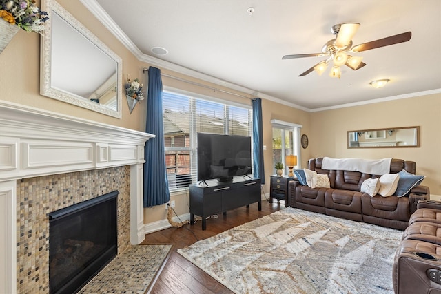 living area with dark wood-type flooring, ornamental molding, a fireplace, and a ceiling fan