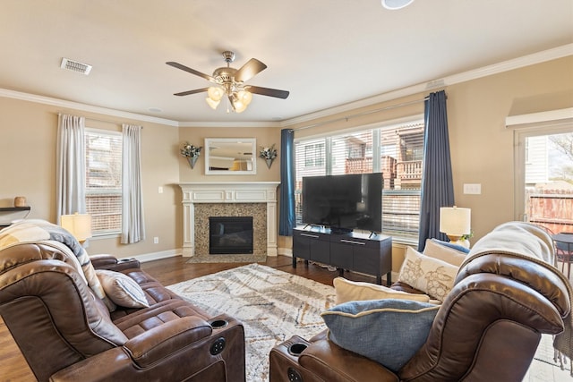 living area featuring visible vents, baseboards, ornamental molding, wood finished floors, and a ceiling fan