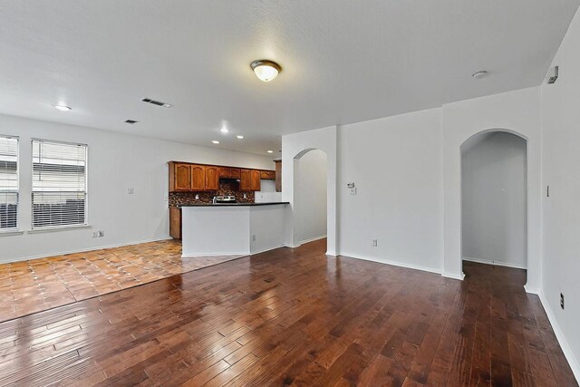 unfurnished living room featuring visible vents, arched walkways, hardwood / wood-style flooring, baseboards, and recessed lighting