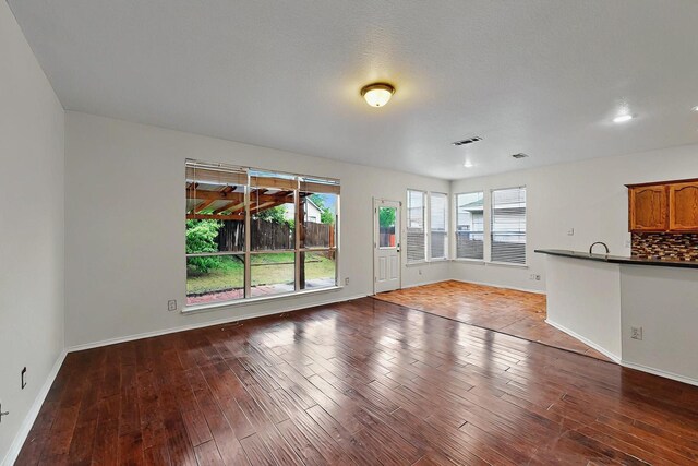 unfurnished living room featuring visible vents, baseboards, a healthy amount of sunlight, and hardwood / wood-style flooring