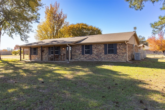 rear view of house with central air condition unit, roof with shingles, fence, brick siding, and a yard