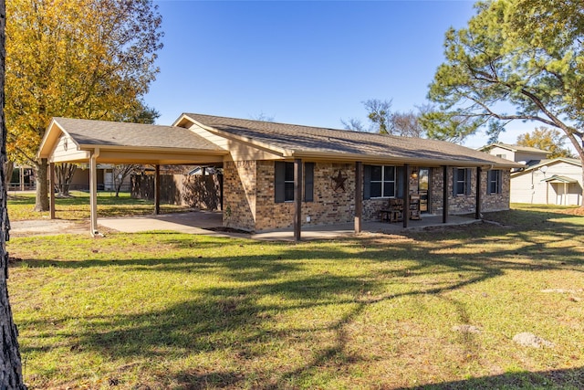 rear view of house featuring an attached carport, brick siding, fence, and a lawn