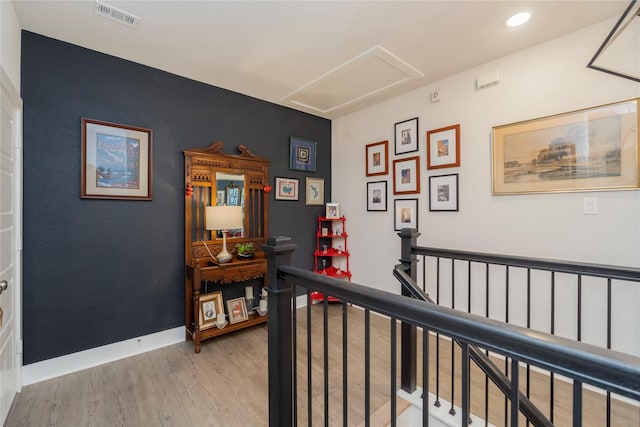 corridor featuring light wood-type flooring, visible vents, attic access, an upstairs landing, and baseboards