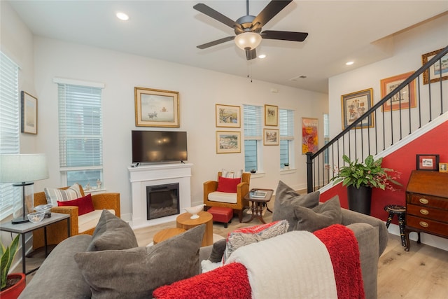 living room with wood finished floors, a ceiling fan, a glass covered fireplace, and stairs