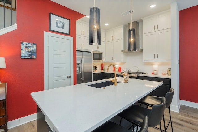 kitchen featuring light countertops, built in appliances, wall chimney exhaust hood, and visible vents