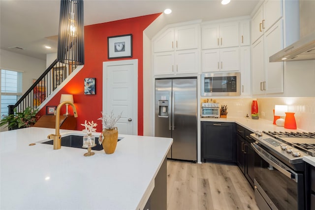 kitchen featuring wall chimney range hood, white cabinetry, appliances with stainless steel finishes, light countertops, and a sink
