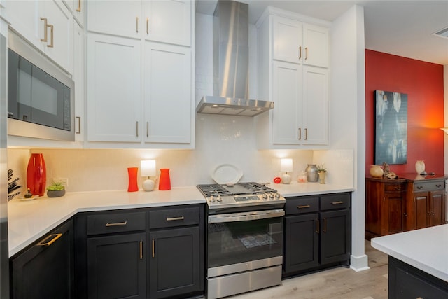 kitchen with light countertops, white cabinetry, built in microwave, wall chimney exhaust hood, and stainless steel gas stove