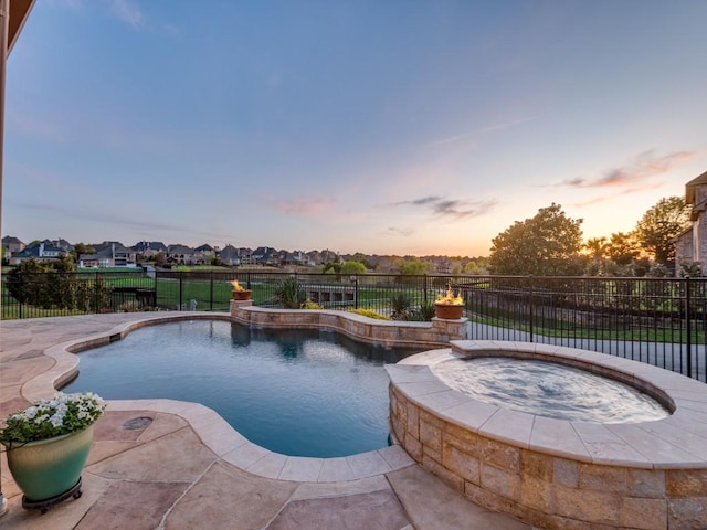 pool at dusk with a residential view, a pool with connected hot tub, a fenced backyard, and a patio area