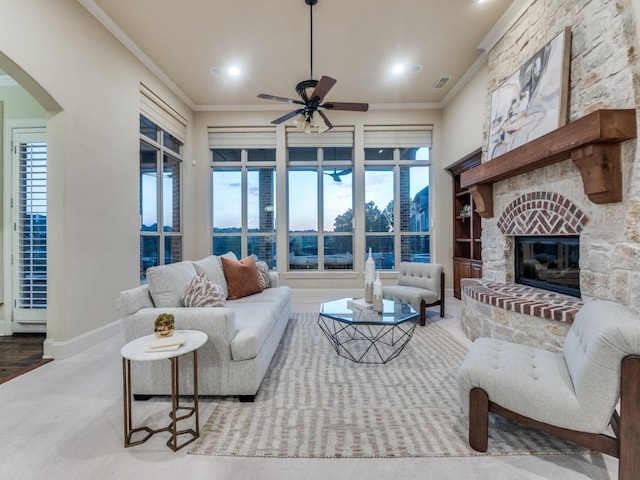 living room featuring arched walkways, visible vents, a ceiling fan, a fireplace, and ornamental molding
