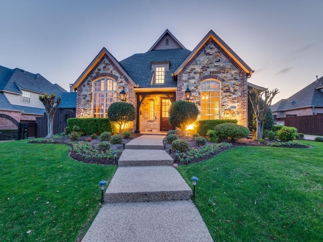 view of front of house with fence, stone siding, a front lawn, and brick siding