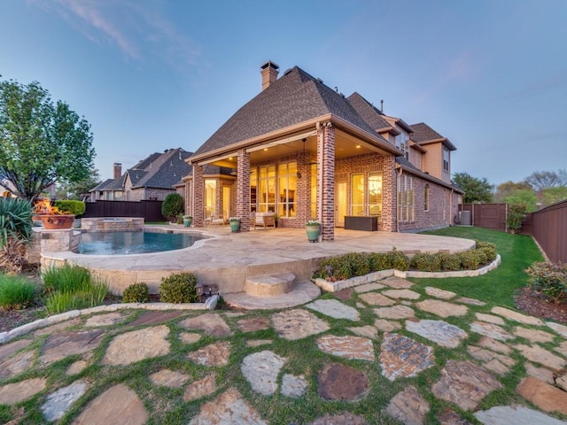 back of property featuring a patio, a chimney, brick siding, a fenced backyard, and a shingled roof