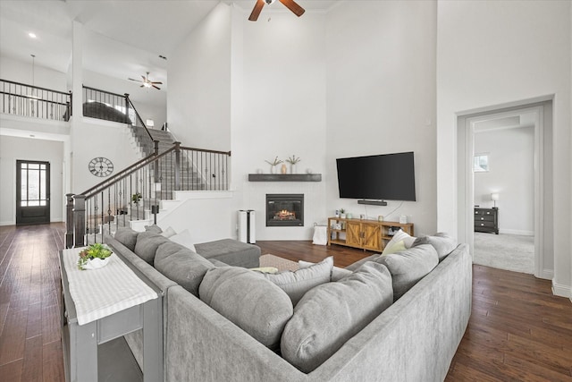 living area with stairs, baseboards, dark wood-style floors, ceiling fan, and a glass covered fireplace