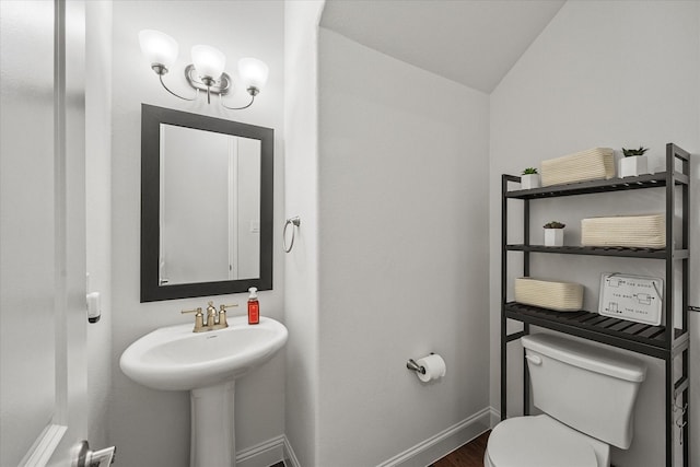 half bathroom with vaulted ceiling, toilet, baseboards, a sink, and wood finished floors