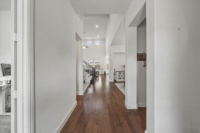 hallway featuring baseboards, dark wood-style flooring, and a towering ceiling