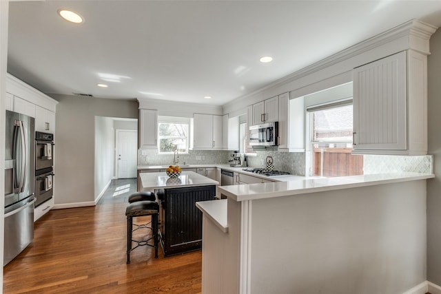 5730 Winton St, Dallas, TX 75206 - kitchen with stainless steel appliances, a peninsula, a breakfast bar area, decorative backsplash, and recessed lighting