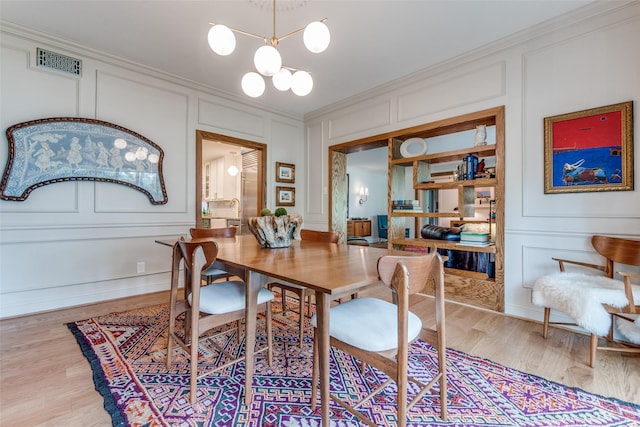 dining space with a decorative wall, crown molding, a chandelier, light wood-type flooring, and visible vents