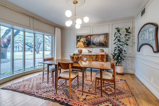 dining room with crown molding, light wood finished floors, a chandelier, and a decorative wall
