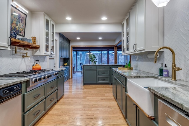 kitchen featuring a sink, light wood-style floors, stainless steel appliances, white cabinetry, and light stone countertops