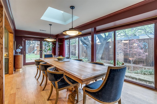dining room featuring light wood-style floors, visible vents, a skylight, and ornamental molding
