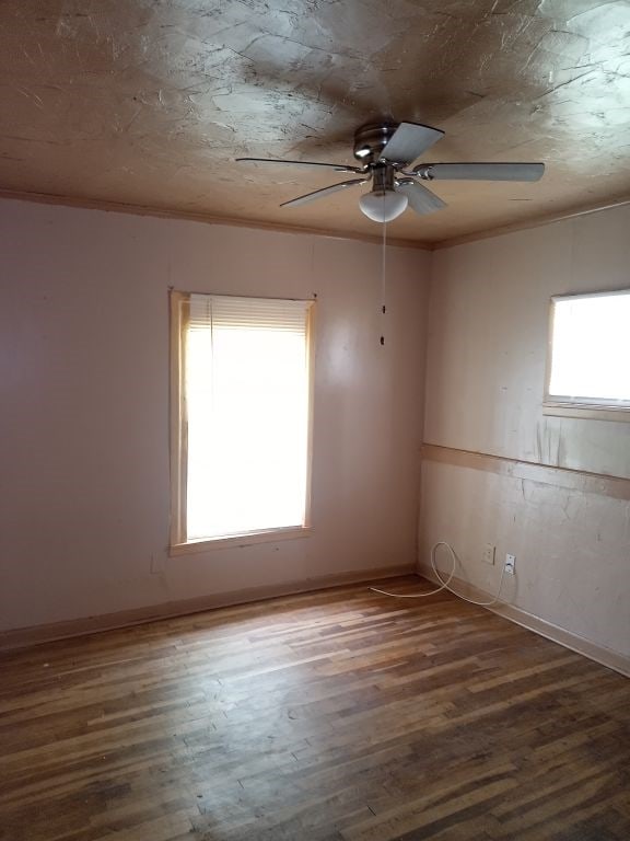 empty room featuring crown molding, baseboards, wood finished floors, and a ceiling fan