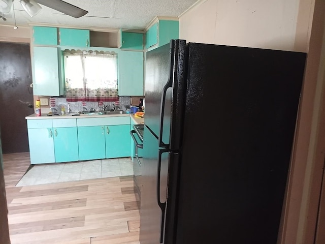 kitchen with a textured ceiling, ceiling fan, a sink, light wood-type flooring, and freestanding refrigerator