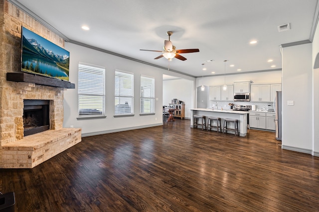 unfurnished living room featuring crown molding, dark wood finished floors, visible vents, a ceiling fan, and a fireplace