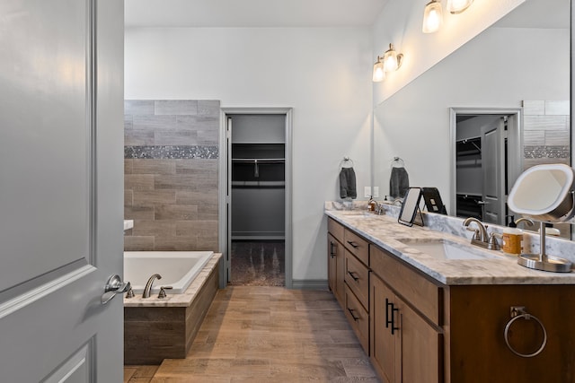 full bathroom featuring a walk in closet, a sink, tiled tub, double vanity, and wood finished floors