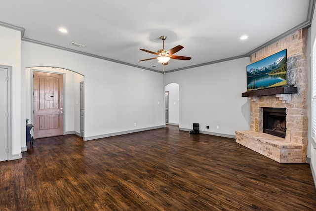 unfurnished living room featuring arched walkways, ceiling fan, crown molding, and a stone fireplace