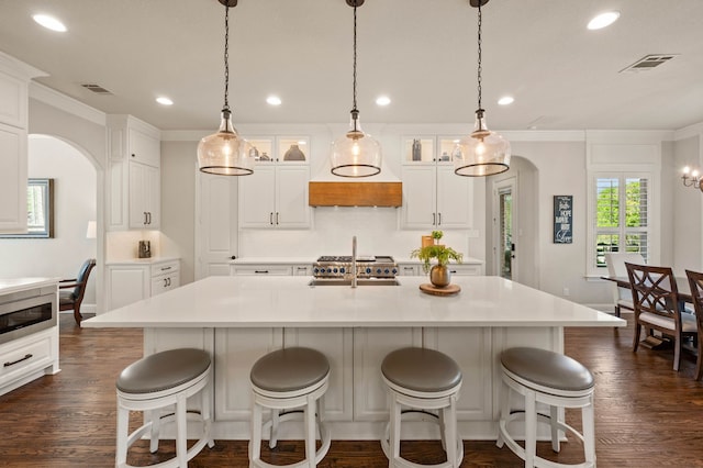 kitchen featuring visible vents, arched walkways, glass insert cabinets, ornamental molding, and recessed lighting