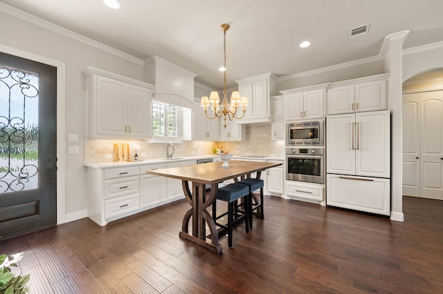 kitchen featuring a sink, built in appliances, white cabinets, and a chandelier