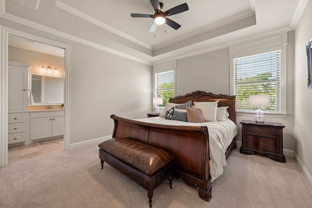bedroom with a tray ceiling, light colored carpet, baseboards, and ensuite bathroom