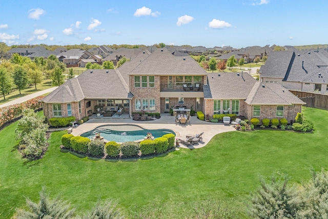 rear view of property with a balcony, a patio, brick siding, a yard, and a residential view
