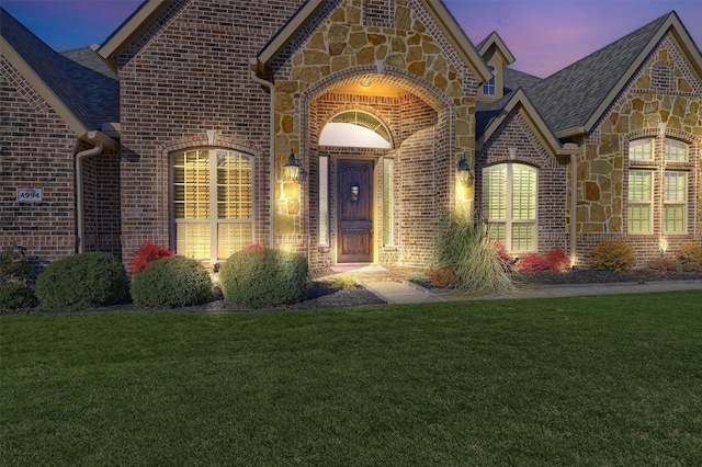 4994 Dogwood Dr, Celina, TX 75009 - exterior entry at dusk with stone siding, brick siding, a yard, and a shingled roof