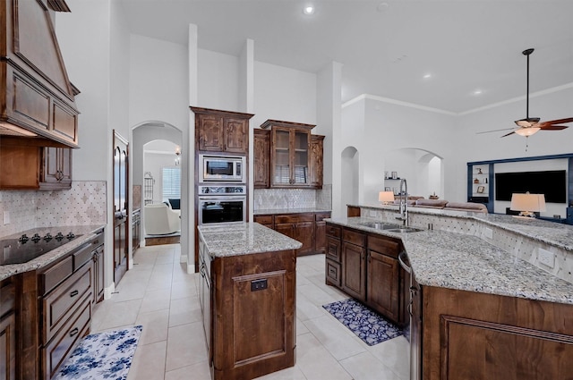 4994 Dogwood Dr, Celina, TX 75009 - kitchen featuring an island with sink, appliances with stainless steel finishes, arched walkways, a ceiling fan, and backsplash