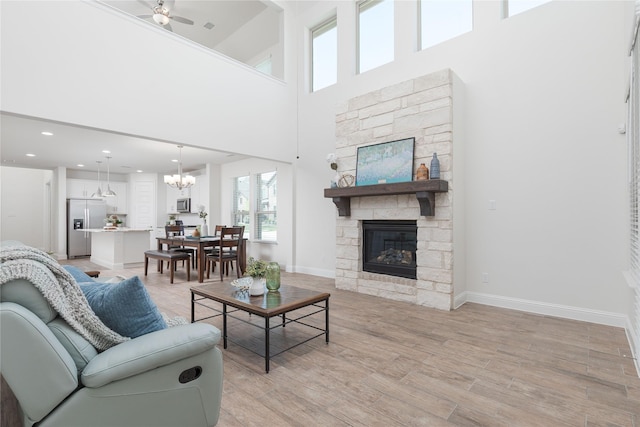 564 Embargo Dr, Fate, TX 75189 - living area featuring a fireplace, baseboards, a towering ceiling, and ceiling fan with notable chandelier